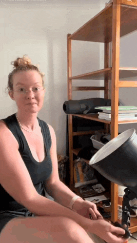 a woman is sitting in front of a wooden shelf holding a black object