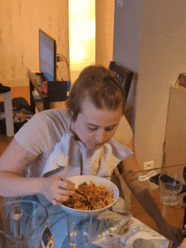 a woman with a towel around her neck is eating a bowl of spaghetti
