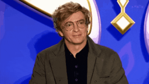 a man wearing glasses and a suit is sitting in front of a blue background