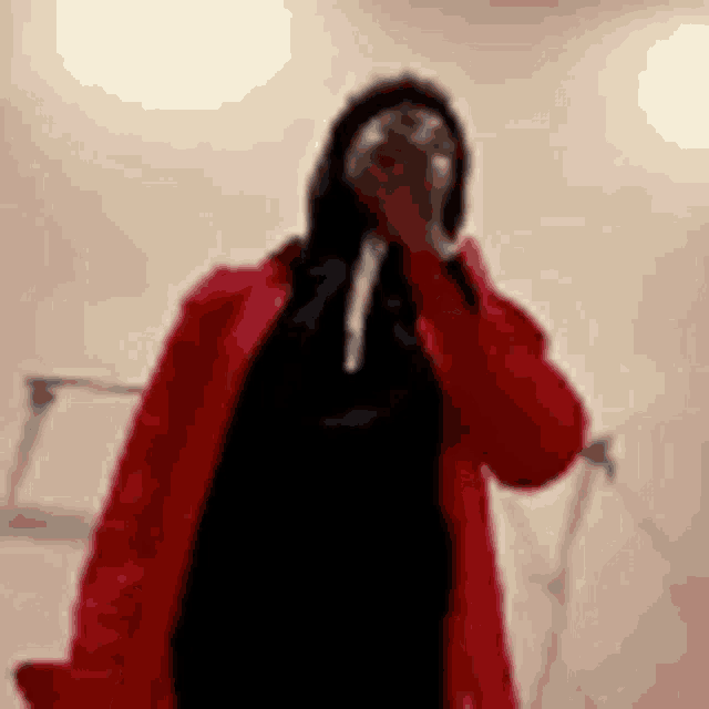 a woman in a red coat is standing in front of a microphone and covering her mouth .