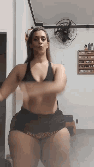 a woman in a black top and shorts is dancing in front of a wall fan
