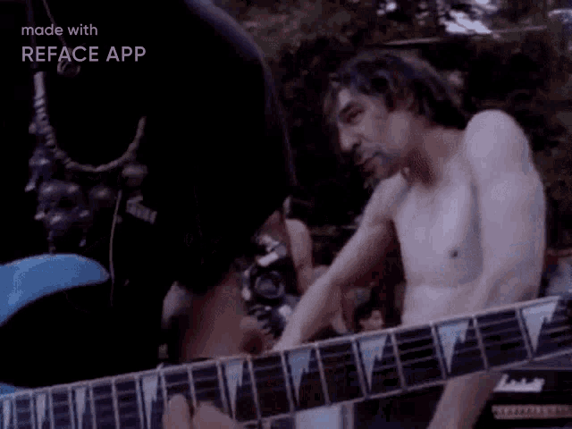 a man is playing a guitar without a shirt on while another man looks on .
