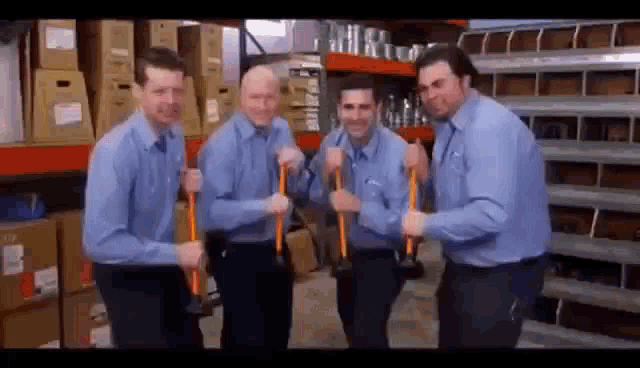 a group of men in blue shirts are standing in a warehouse holding hammers .