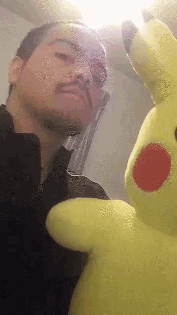 a man with a beard is holding a yellow pikachu stuffed animal