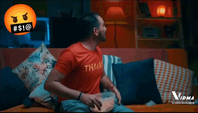 a man sitting on a couch wearing a red shirt that says " than "