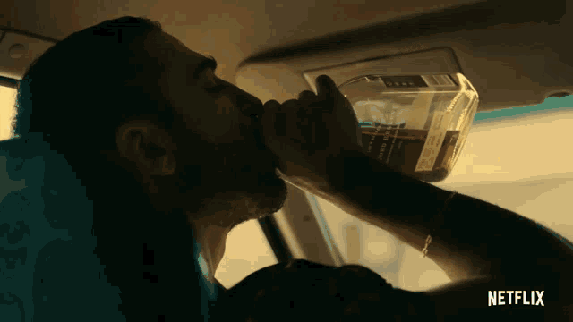 a man drinking from a bottle in a car with netflix on the bottom right