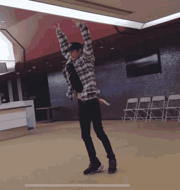 a man in a plaid shirt is dancing in a room with empty chairs