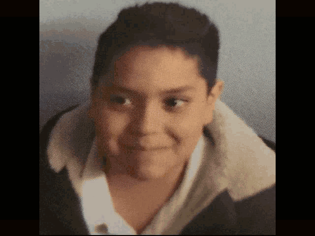 a young boy wearing a white shirt and a black jacket is smiling .