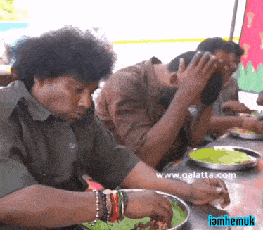 a group of men are sitting at a table with plates of food and the website www.galatta.com is on the bottom right