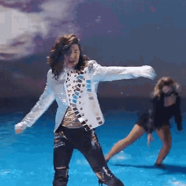 a man in a white jacket is dancing on a blue stage