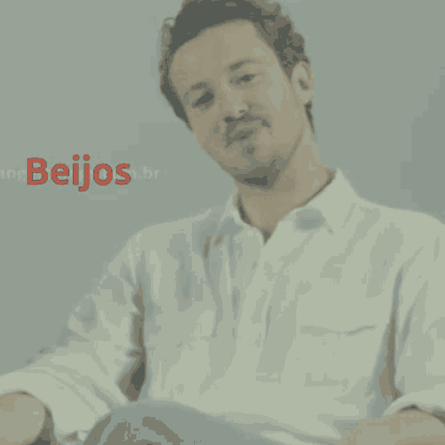a man in a white shirt is sitting in front of a sign that says beijos