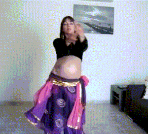 a pregnant woman is dancing in a living room with a picture on the wall behind her