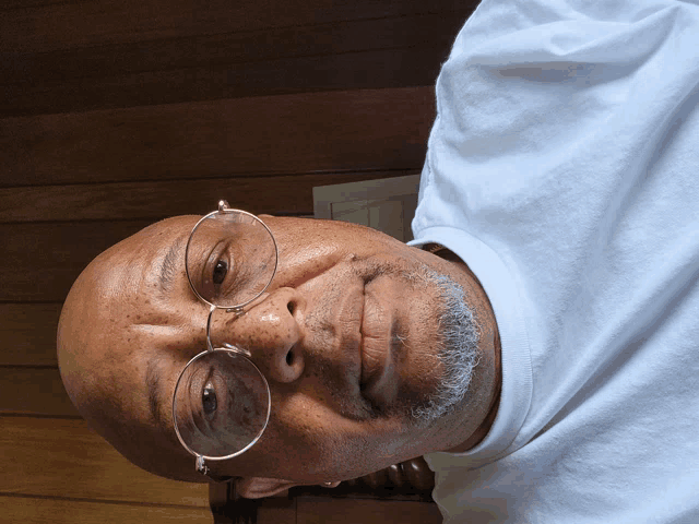 a man wearing glasses and a white shirt looks down at the camera