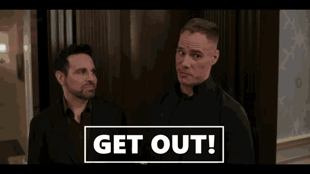 two men are standing next to each other with a sign that says " get out "