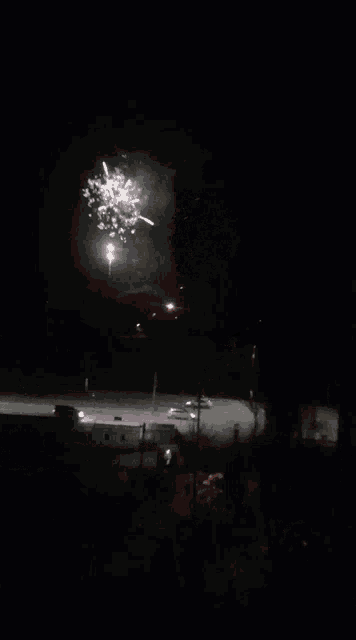a fireworks display is visible over a parking lot at night