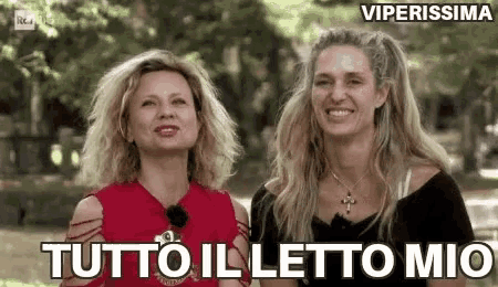 two women are standing next to each other in a park and smiling at the camera .