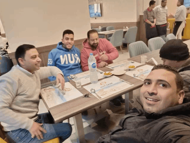 a man wearing a blue sweatshirt that says ' co ' on it sits at a table with other men