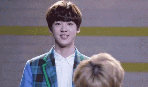 a young man in a plaid jacket and white shirt is making a funny face while standing next to another young man .
