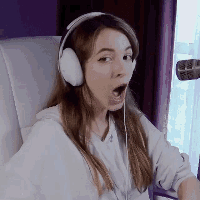 a woman wearing headphones is sitting in a chair and making a surprised face .