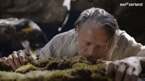 a man is laying on the ground with his mouth open and smelling moss .