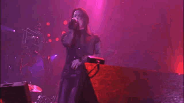 a man singing into a microphone on a stage with a purple light behind him