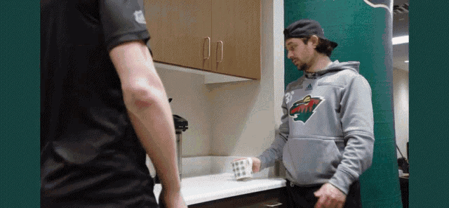 a man wearing a minnesota wild sweatshirt is standing in a kitchen