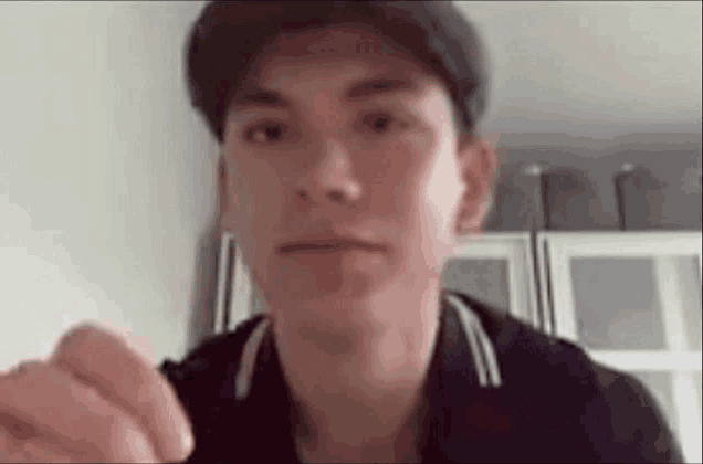a young man wearing a hat and a black jacket is making a funny face while looking at the camera .
