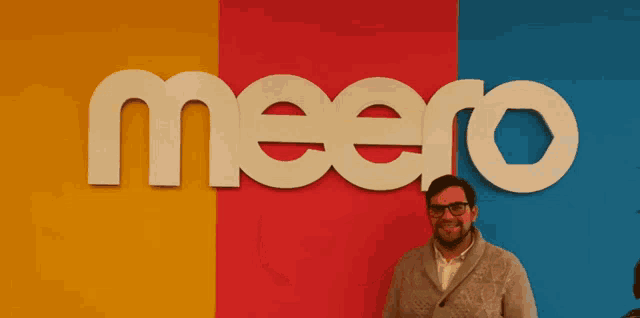 a man stands in front of a meero sign holding a yellow book