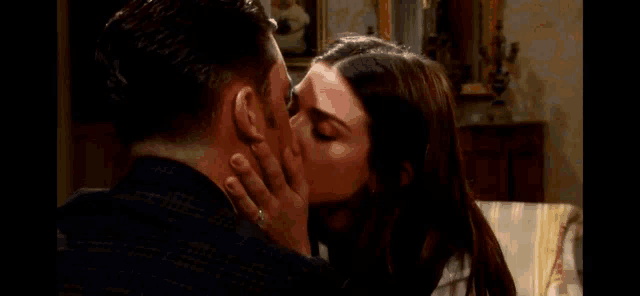 a man and a woman are kissing in a living room while sitting on a couch .