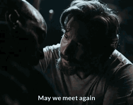 a man with a beard is talking to another man in a dark room and the words may we meet again are visible .