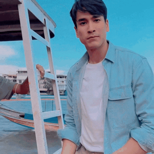 a man wearing a blue shirt and white t-shirt stands in front of a boat that says ' bangkok ' on it