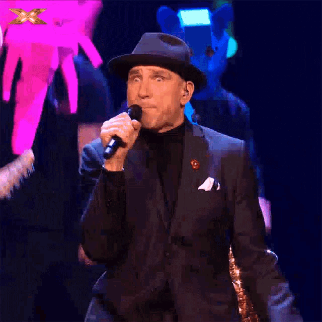 a man in a suit and hat singing into a microphone on a stage