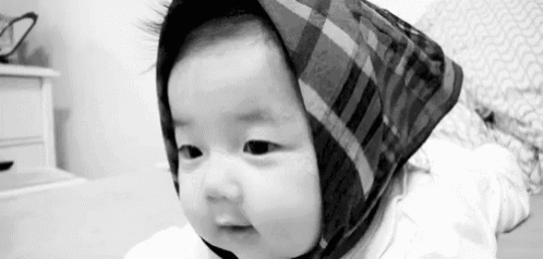 a black and white photo of a baby wearing a plaid scarf on its head .