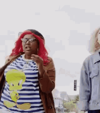 a woman with red hair and glasses is standing next to another woman wearing a tweety bird shirt .