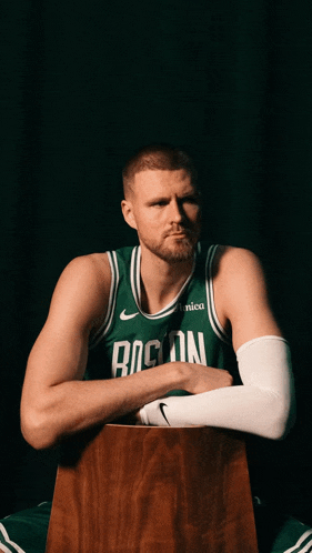 a boston celtics player sits on a wooden box