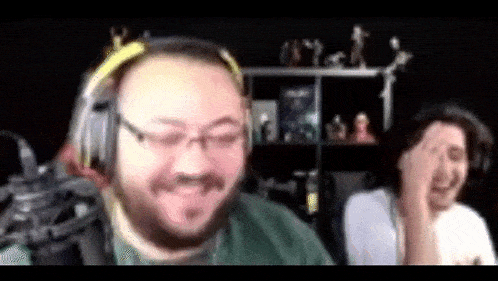a man wearing headphones and glasses is laughing while another man covers his face .