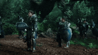 a man in armor is standing in the middle of a forest with a sword .