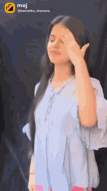 a girl in a blue shirt is making a funny face with her hand on her forehead