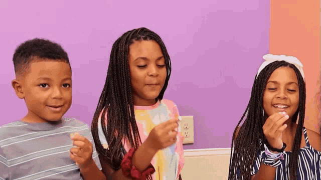 a boy and two girls are standing in front of a pink wall