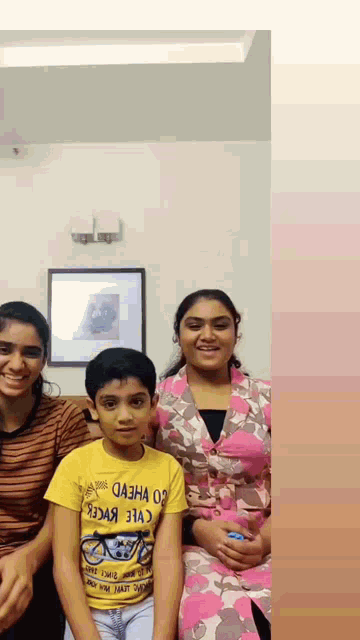 a boy wearing a yellow shirt with a bicycle on it poses for a picture with two women