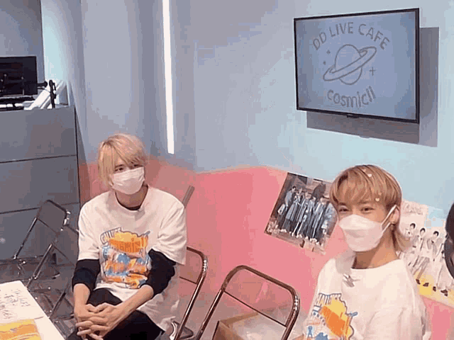 two people wearing face masks are sitting in front of a sign that says dd live cafe