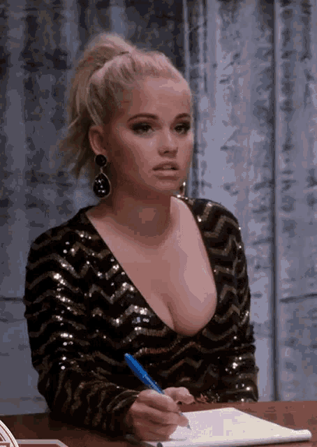 a woman in a sequined top is sitting at a desk writing in a notebook