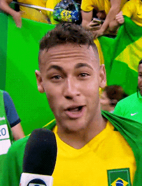 a man in a yellow shirt is talking into a microphone with a green flag behind him