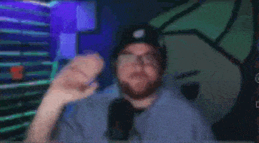 a man with a beard and glasses is sitting in front of a microphone and waving .