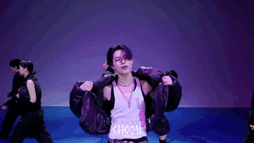a man with purple hair is holding a jacket over his shoulder while a group of people are dancing in the background .
