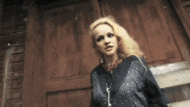 a woman with blonde hair is standing in front of a wooden building