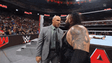 a man in a suit and tie stands next to another man in a wrestling ring with the word raw on the wall