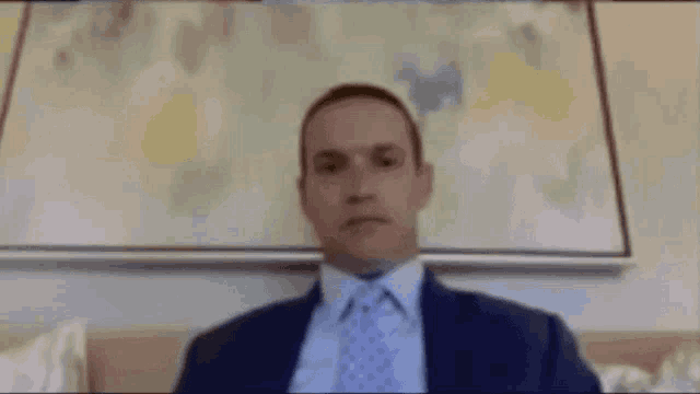 a man in a suit and tie is sitting in front of a painting on the wall .