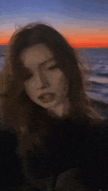 a blurry picture of a woman taking a selfie in front of the ocean at sunset .