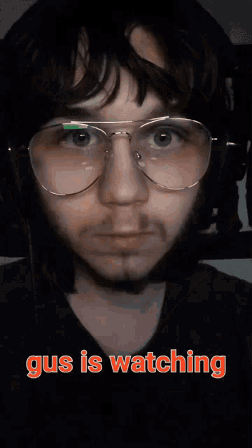a close up of a man 's face with glasses and the words gus is watching below him